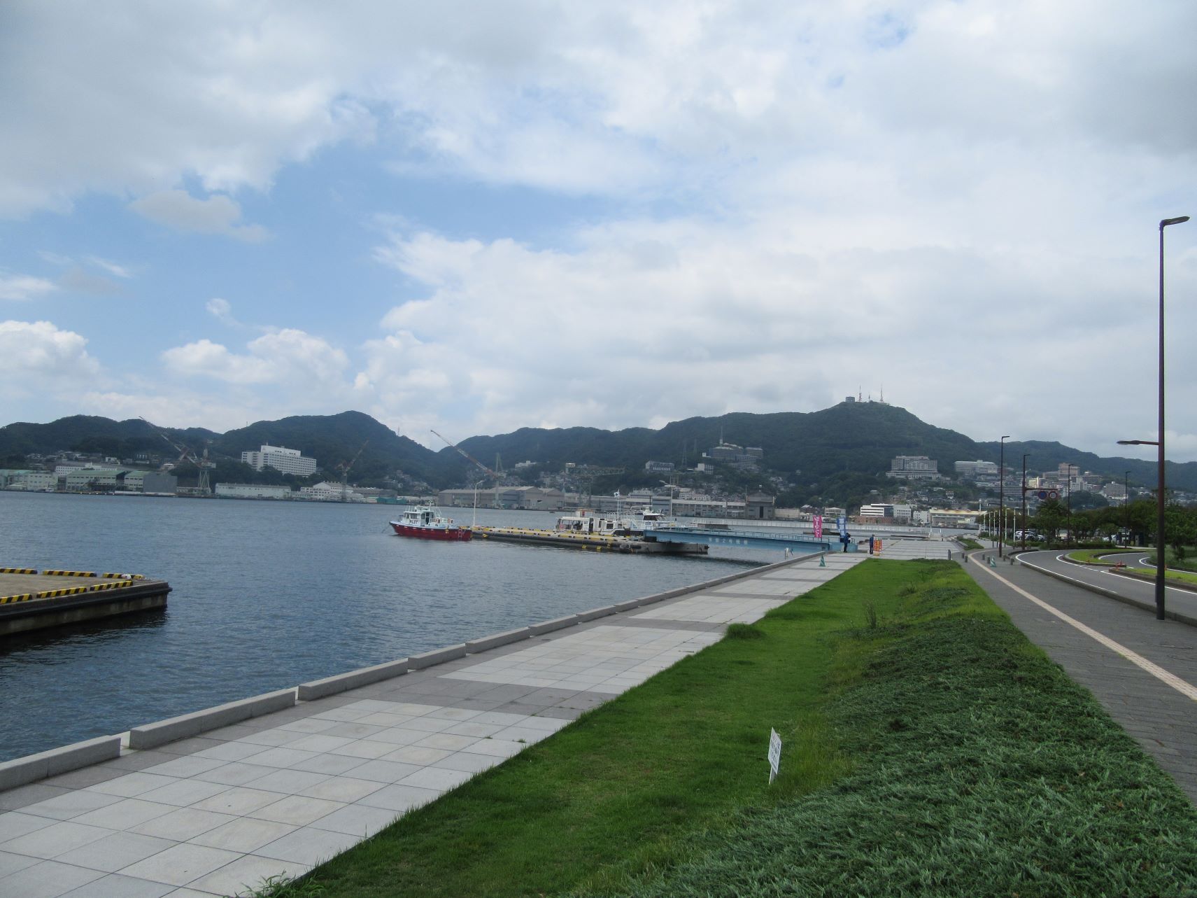 長崎市・長崎水辺の森公園周辺の海辺の道。奥に見えるのは稲佐山。